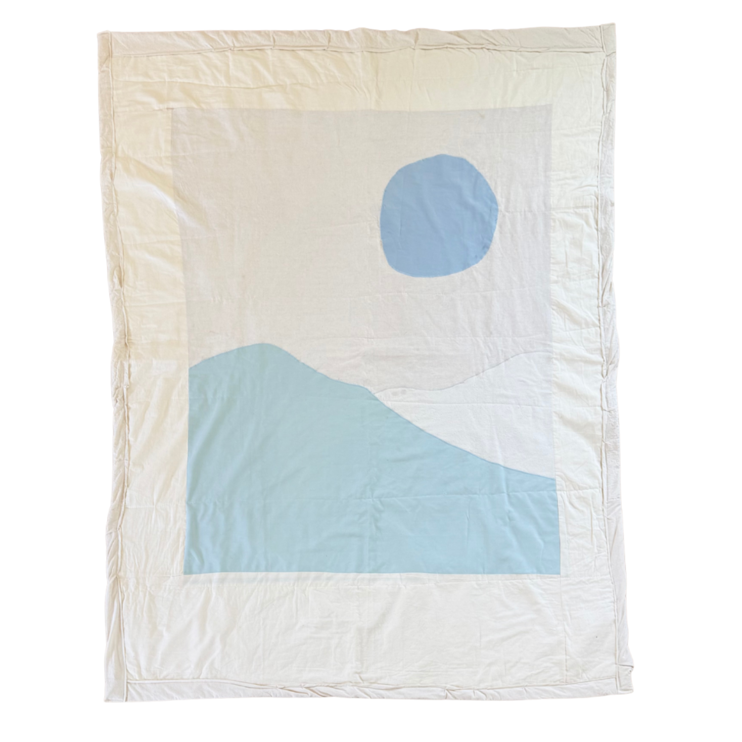 A quilt with a simple design of a mountain and a circle, with the mountain in soft blue and the circle, representing the sun or moon, in matching light blue on a white background.