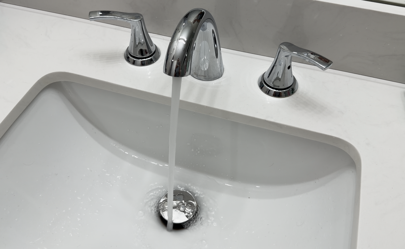 A white bathroom sink with a silver faucet and handles, with water flowing from the faucet.