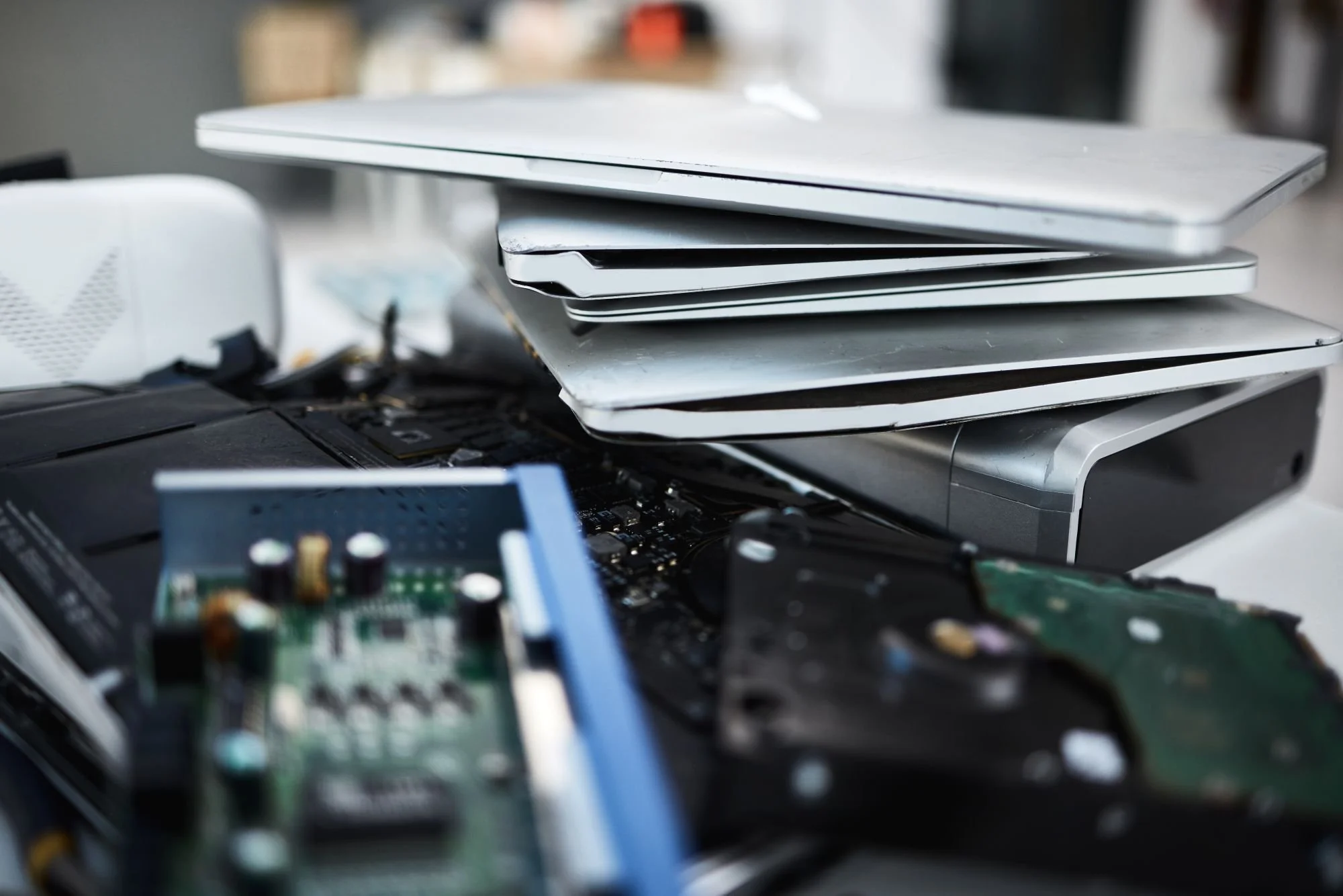 A stack of laptops and electronic circuit boards placed on a cluttered surface.