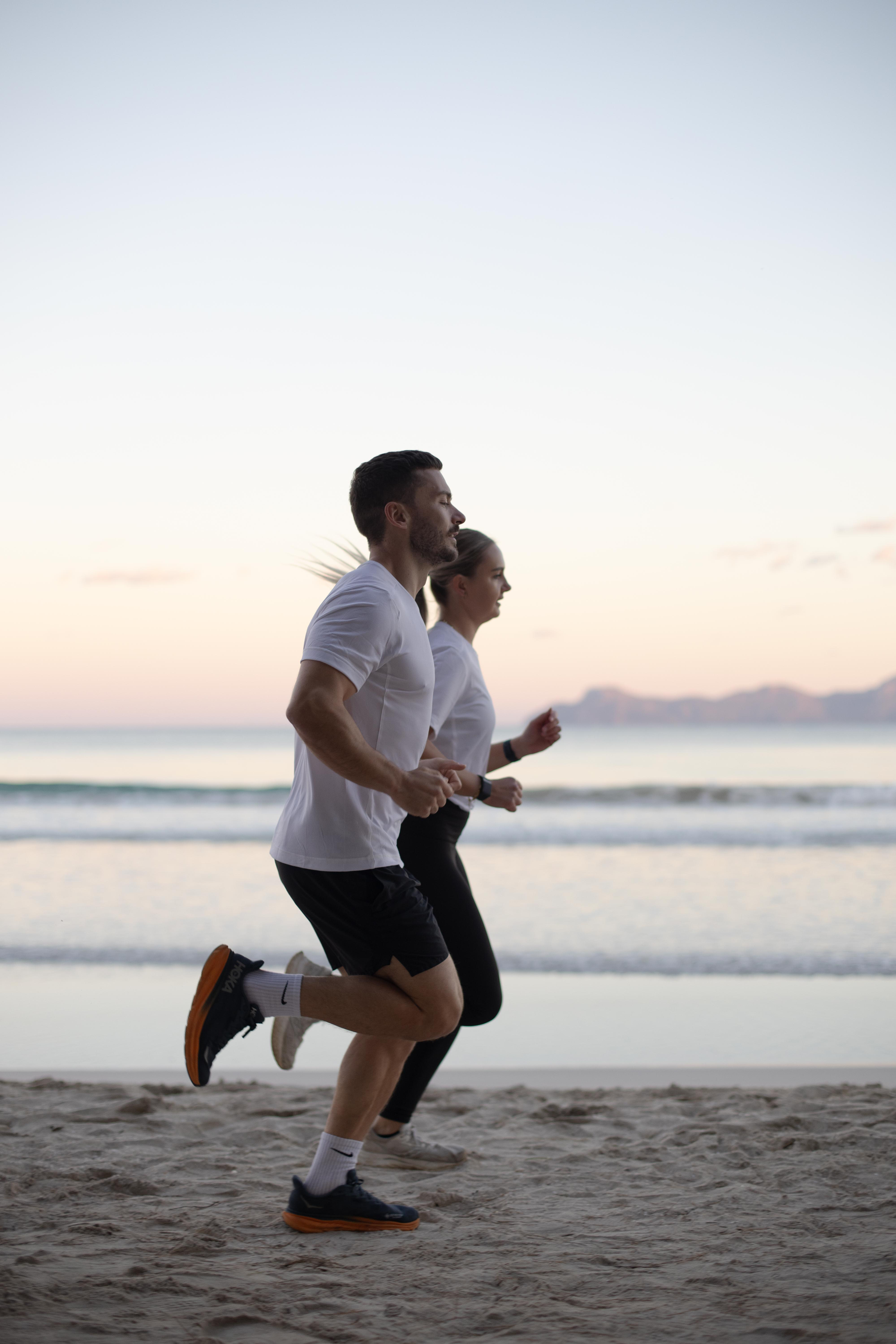 A man and a woman jogging on the beach at sunset.