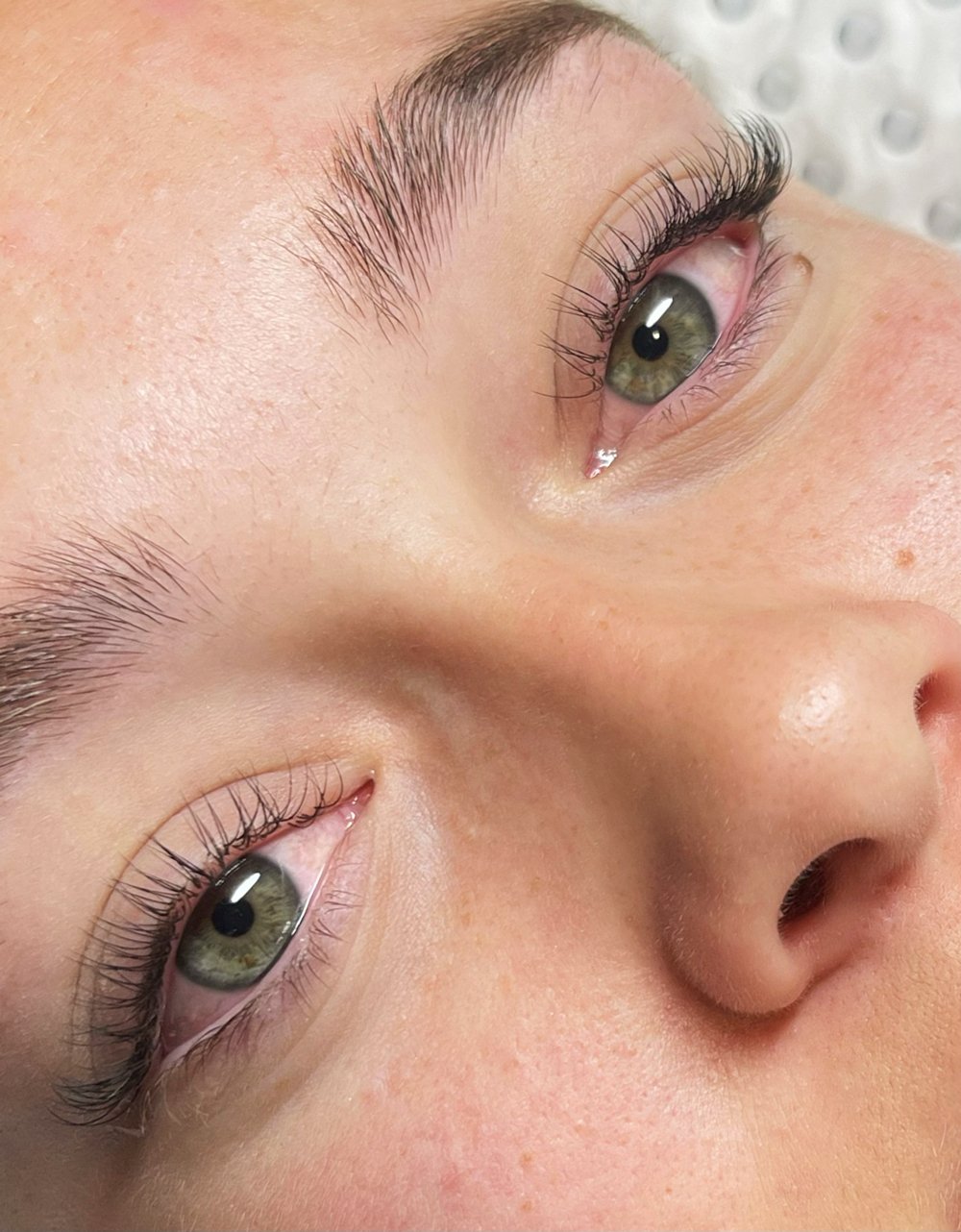 Close-up of a person's face, focusing on green eyes with long eyelashes and well-groomed eyebrows, and part of the nose.