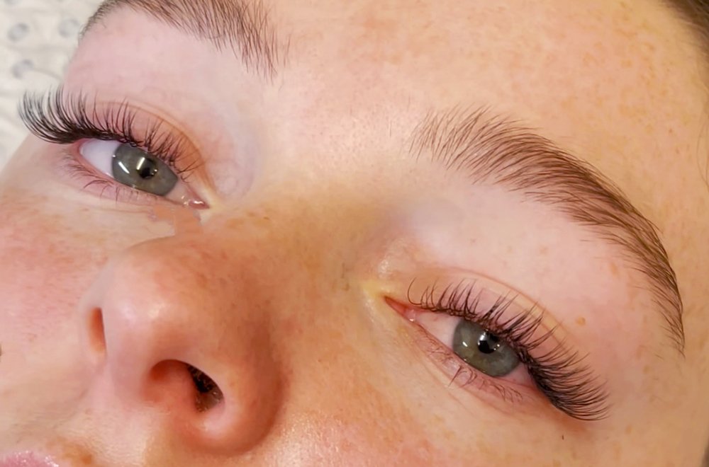 Close-up of a person with blue eyes, freckles, and long eyelashes, lying down with eyes partially closed.