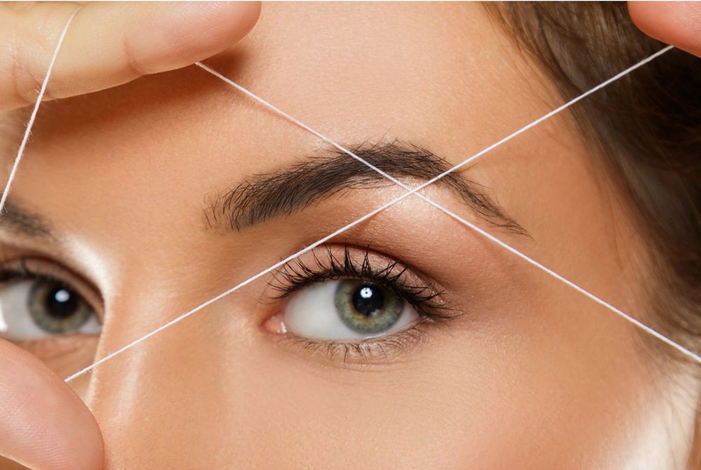 Close-up of a woman's face with strings crossing her eyebrows,  illustrating eyebrow threading