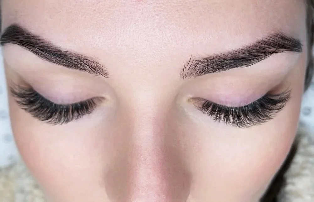Close-up of a woman's face with eyelash extensions and groomed eyebrows, eyes closed.