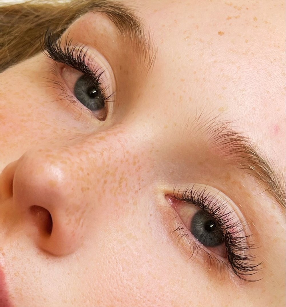 Close-up of a person's face showing their blue eyes, long eyelashes, freckles, and light eyebrows.