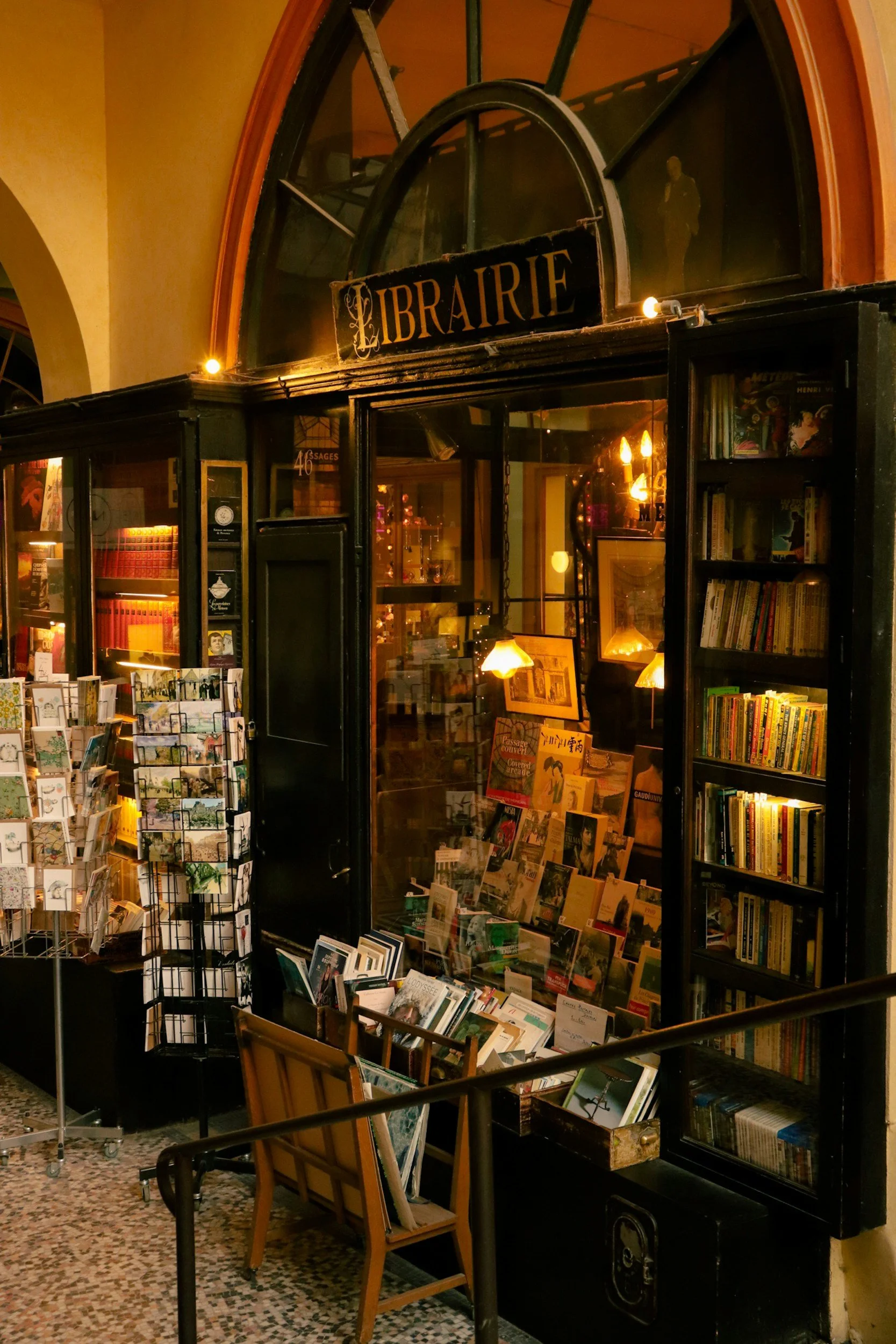 A vintage bookstore with a black exterior, shelves filled with books, postcards, and artwork, and a sign that reads 'Librairie' under an arched window.