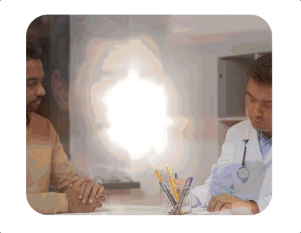 A doctor in a white coat and stethoscope sitting across from a woman in a beige shirt at a desk, with a bright light in the background.