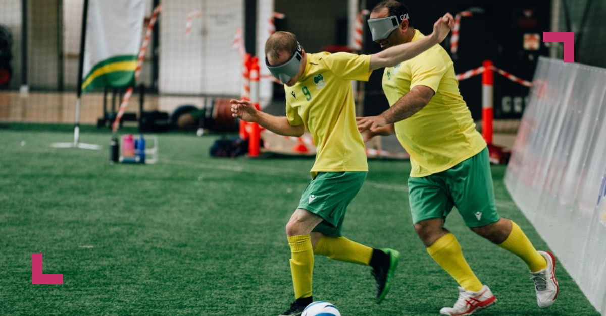 A photo of two middle aged men playing football/soccer in their green and gold jerseys. They are wearing blind folds.