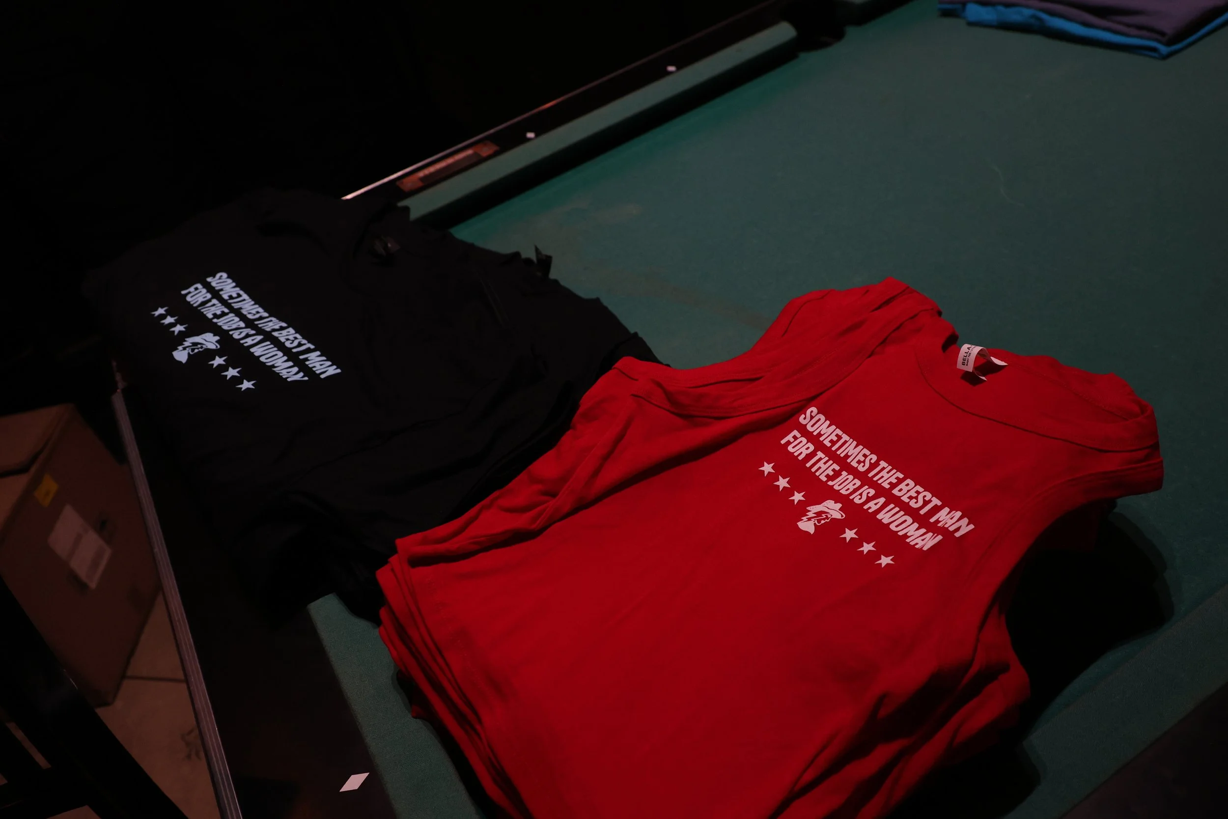 Red and black T-shirts with printed slogans, laid on a table in a store.