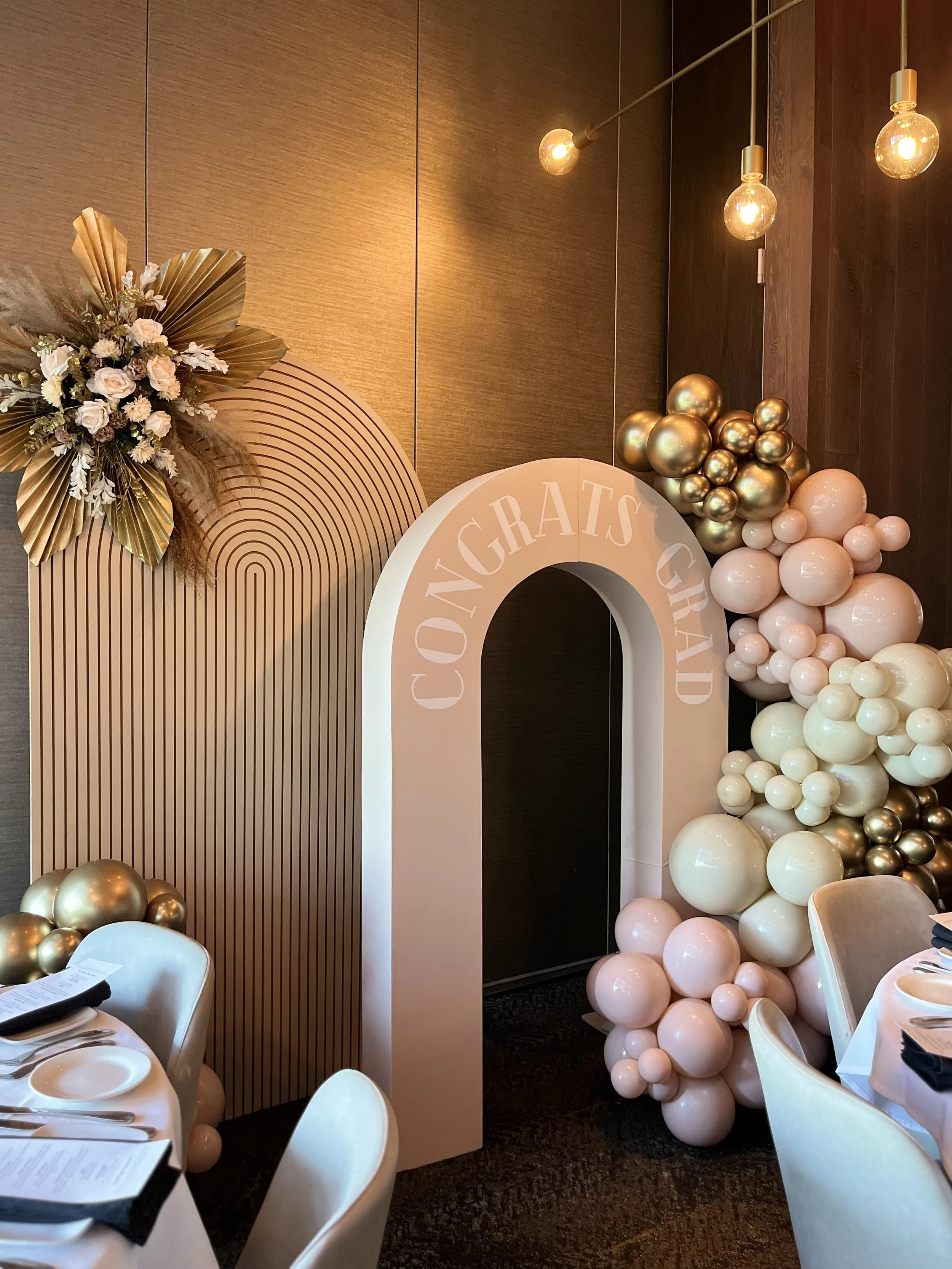 Decorative birthday celebration setup with a balloon arch and a sign that reads "CONGRATS GRAD" in an event space.