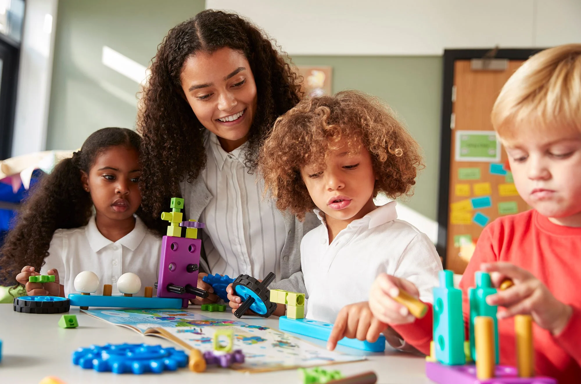Teacher helping children build with colorful educational toys in classroom.