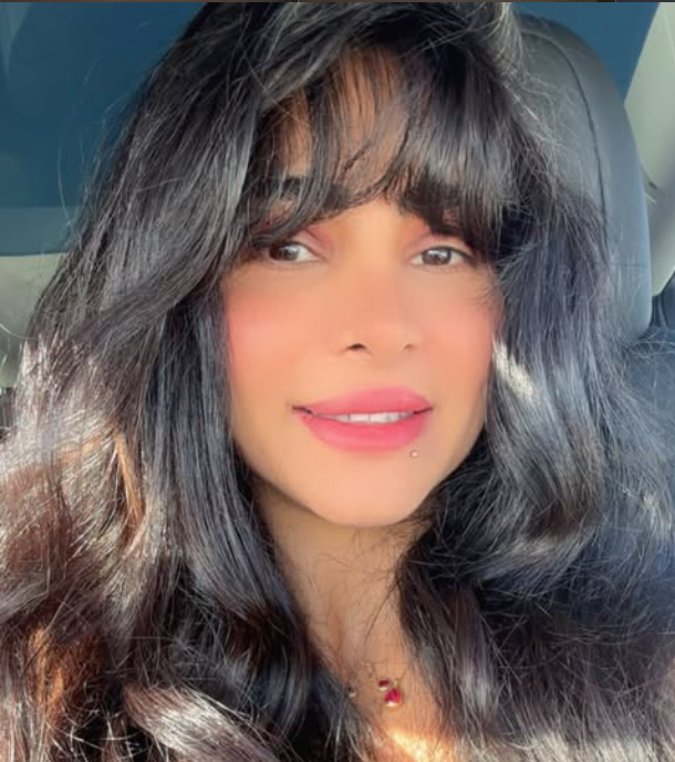 A woman with long, dark hair and bangs smiling in a car.