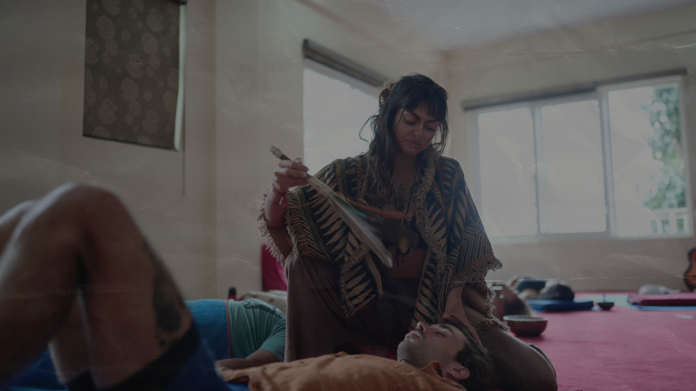 People lying on yoga mats inside a bamboo structure, participating in a yoga or meditation session, with an instructor standing nearby.