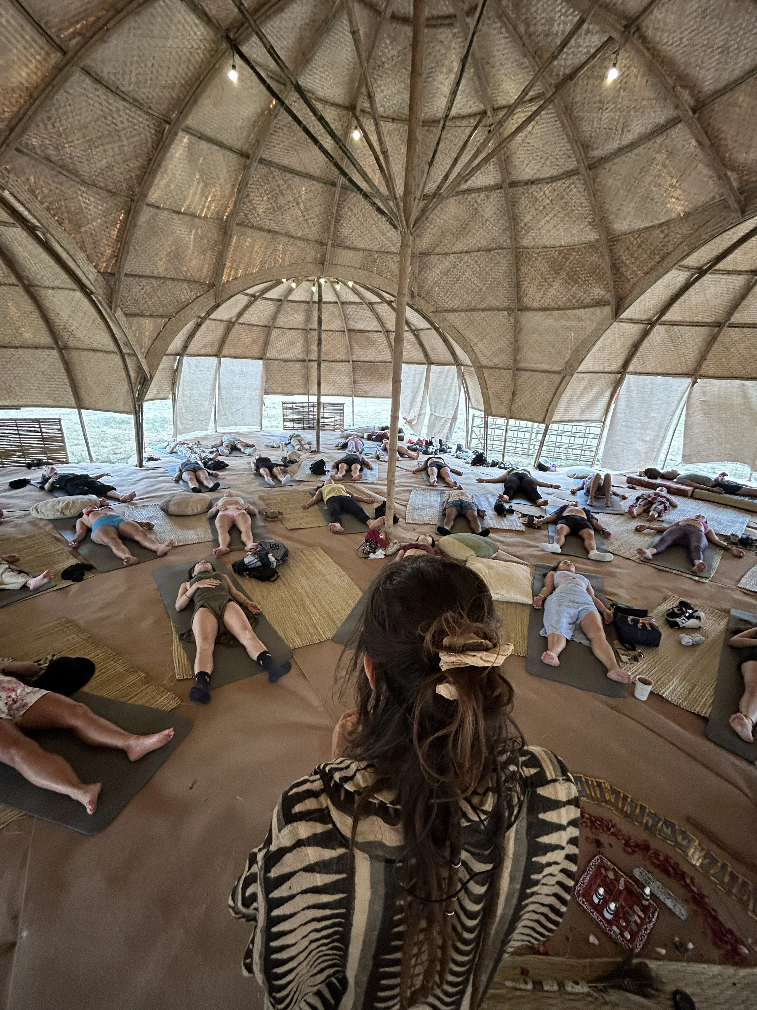 People participating in a breathwork session by Kaylani inside a large bamboo structure, lying on mats and resting.
