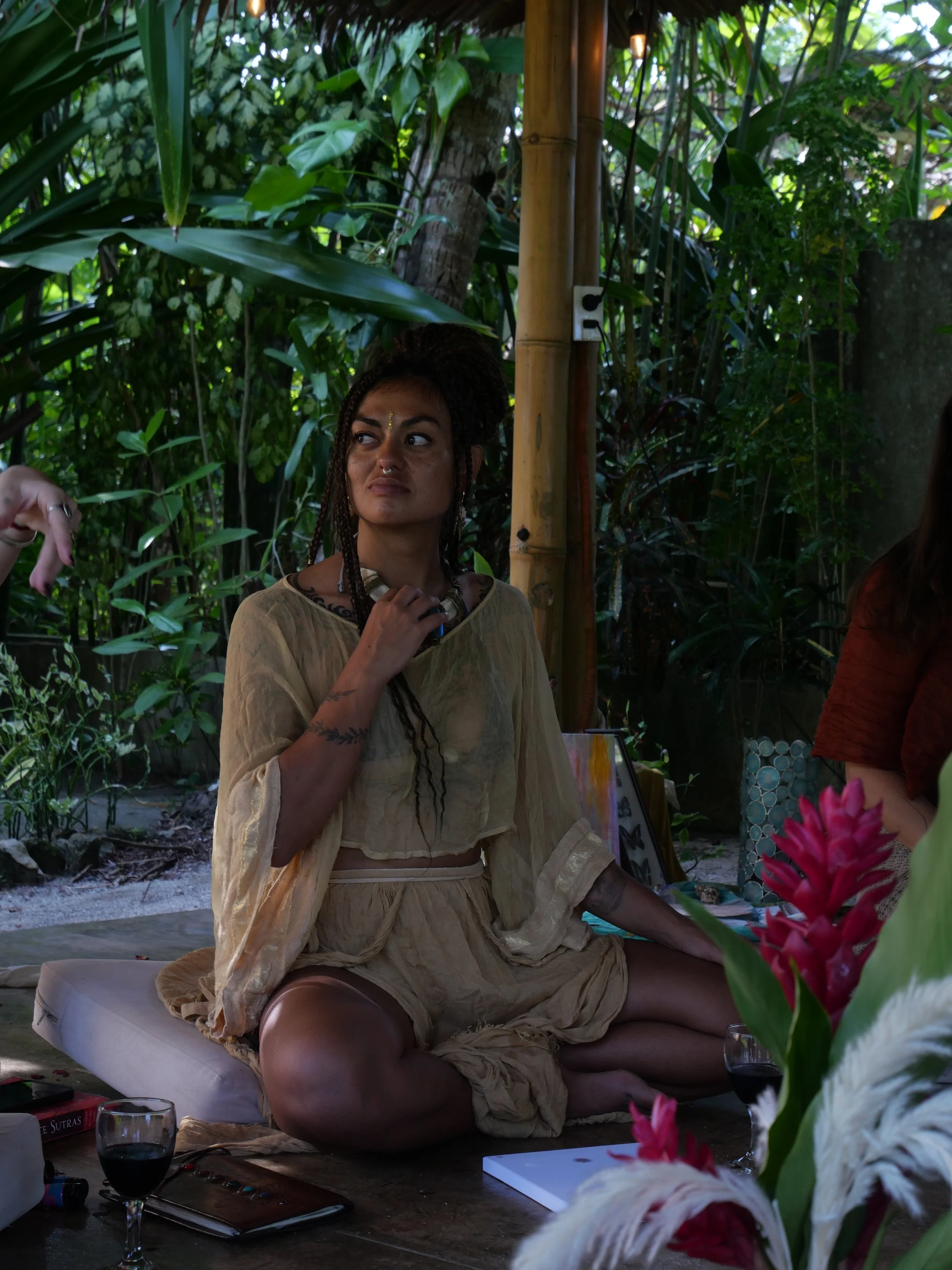 Kaylani seated cross-legged on a cushion, in a jungle setting during a retreat she co-hosted, looking to the side with a contemplative expression.