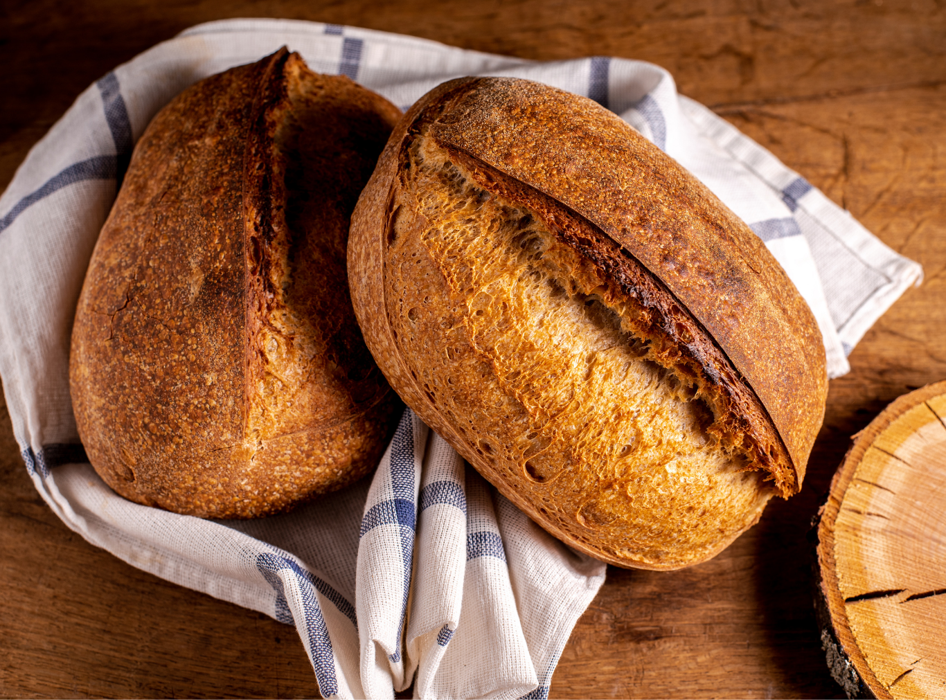 Heritage Hearth Sourdough loaf wrapped in a linen tea towel, sitting on a flour-dusted cutting board alongside a serrated bread knife.