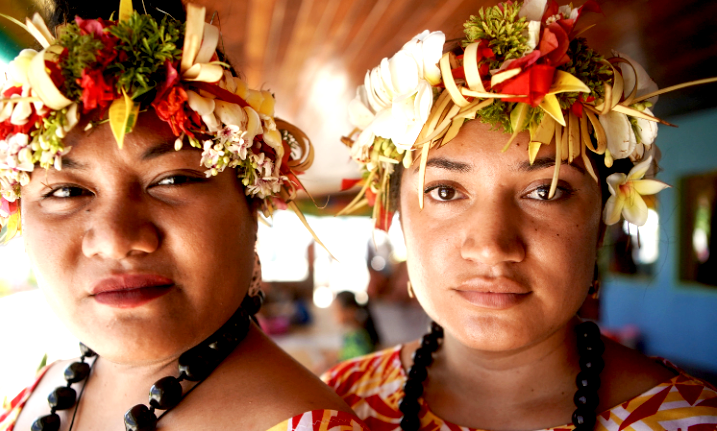 Two young Tuvaluan women wearing vibrant traditional floral garlands (fau), representing the living culture and heritage bread traditions of the 11,000 people living on the front lines of climate change.
