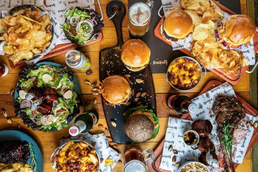 Overhead view of a spread of standard American diet foods, including burgers, fries, and fried appetizers, representing the processed food choices discussed in the 'Real Food Truth' blog post.