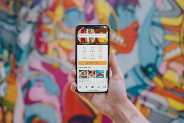 A person holding a smartphone and using a food scoring app to scan a product barcode in front of a vibrant, artistic wall, illustrating the use of consumer tools like Yuka to decode food additives and nutritional quality.