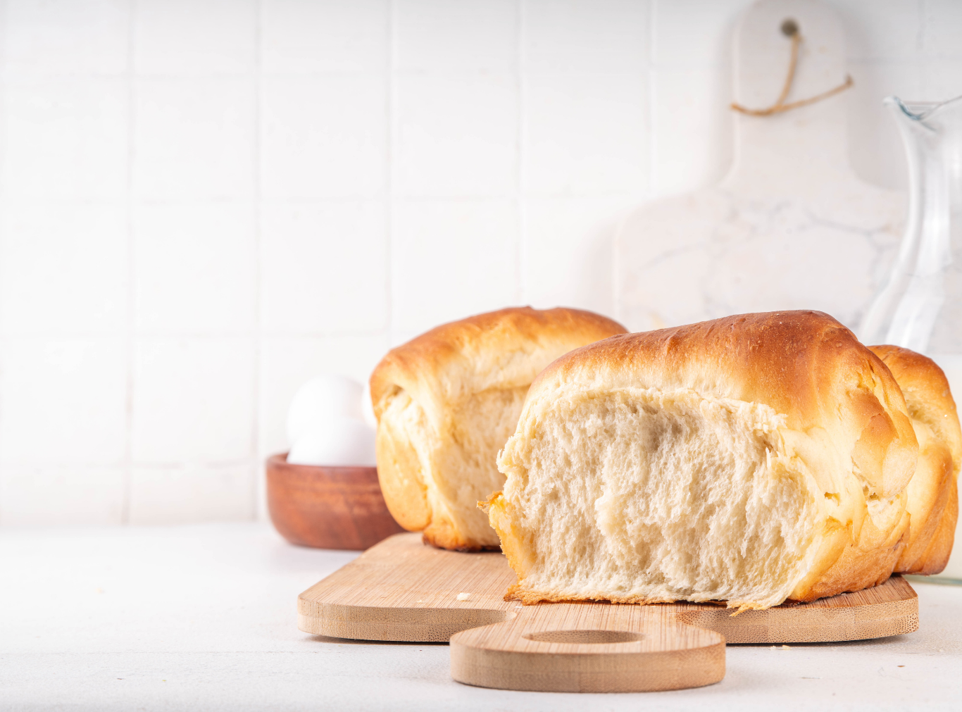 Close-up of a golden-brown loaf of Pillowy Milk Bread, showing its soft, shredded texture as a piece is pulled away.