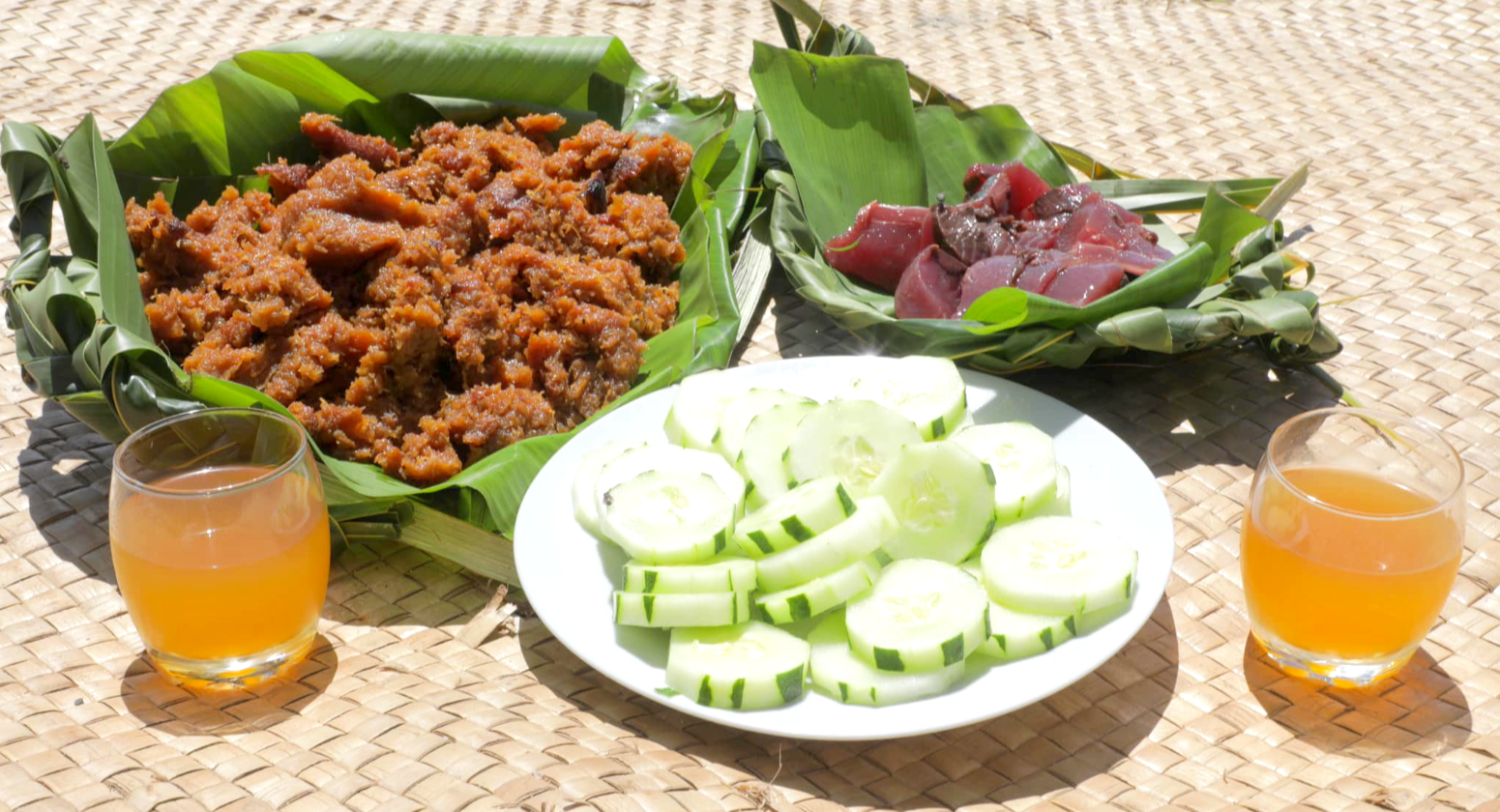 A traditional Tuvaluan meal on a woven mat featuring Fekei Pulaka (taro pudding), raw tuna, and a glass of sweet kaleve coconut toddy, representing the unique fermentation heritage of the atolls.