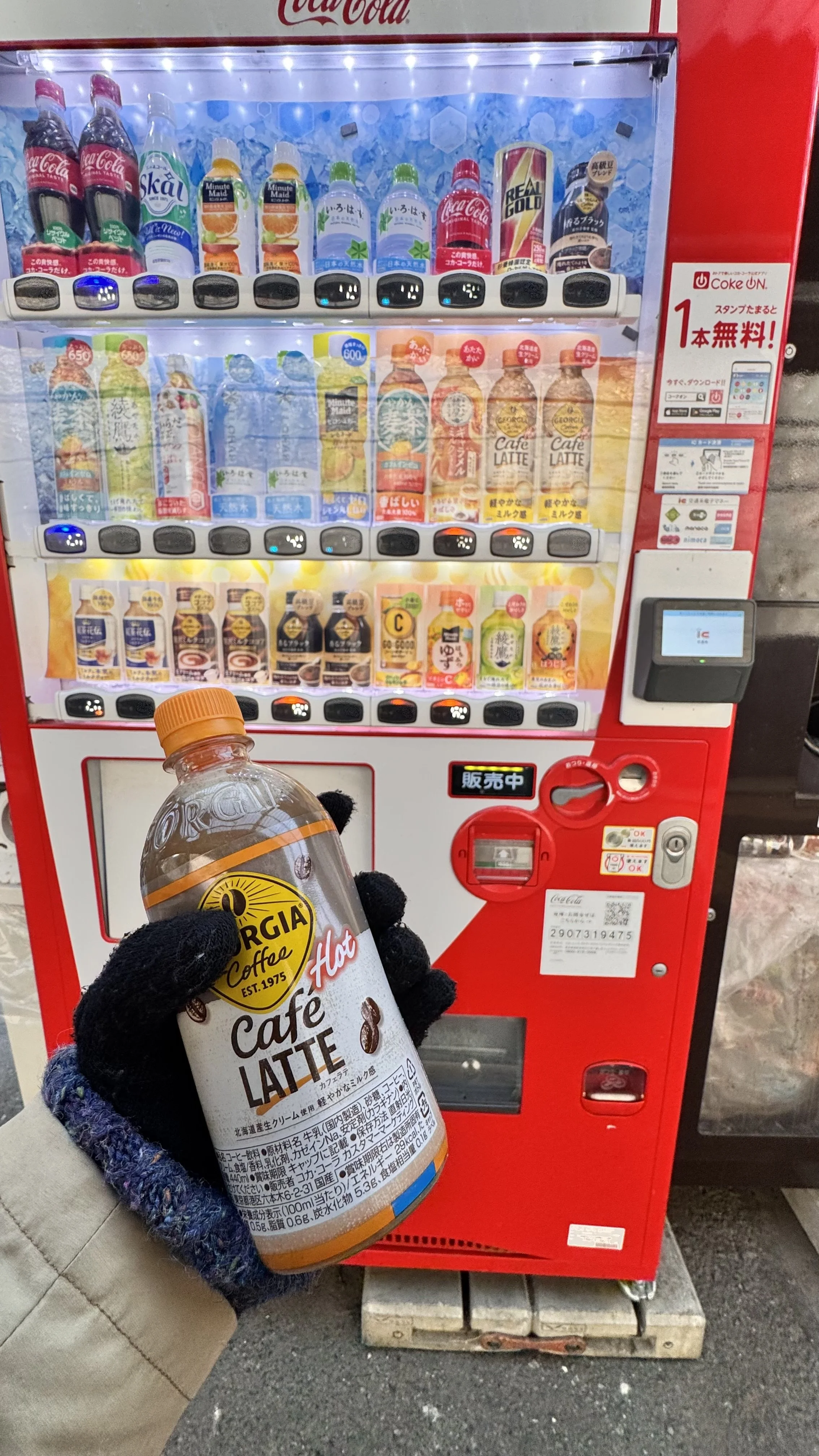 Pessoa segurando uma garrafa de café latte quente ao lado de uma máquina de venda automática de bebidas no Japão.
