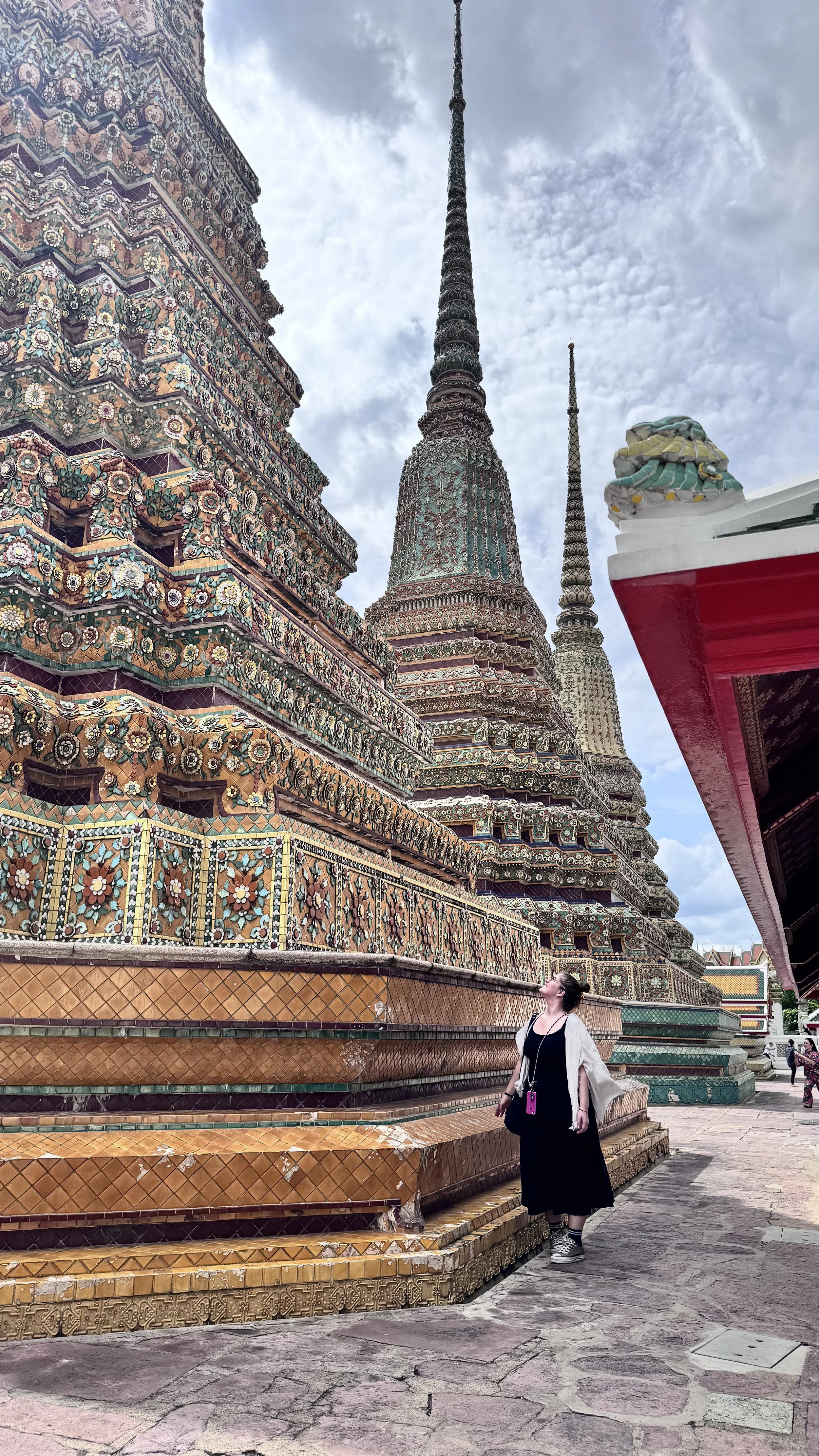Pessoa observando um templo decorado com mosaicos coloridos e detalhes ornamentais. O templo possui torres altas contra um céu parcialmente nublado.