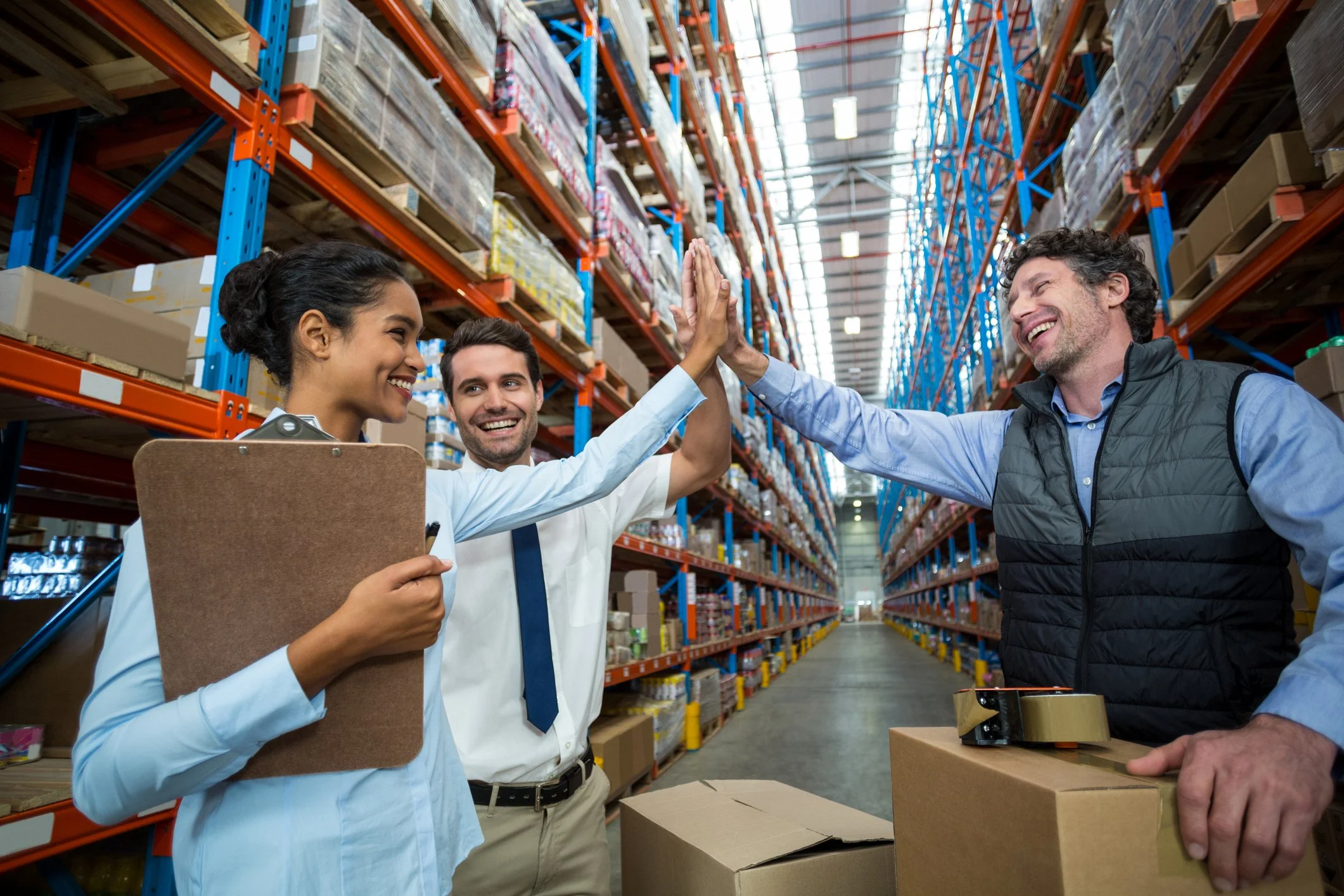 Three warehouse workers high-five each other amidst shelves stocked with boxes.