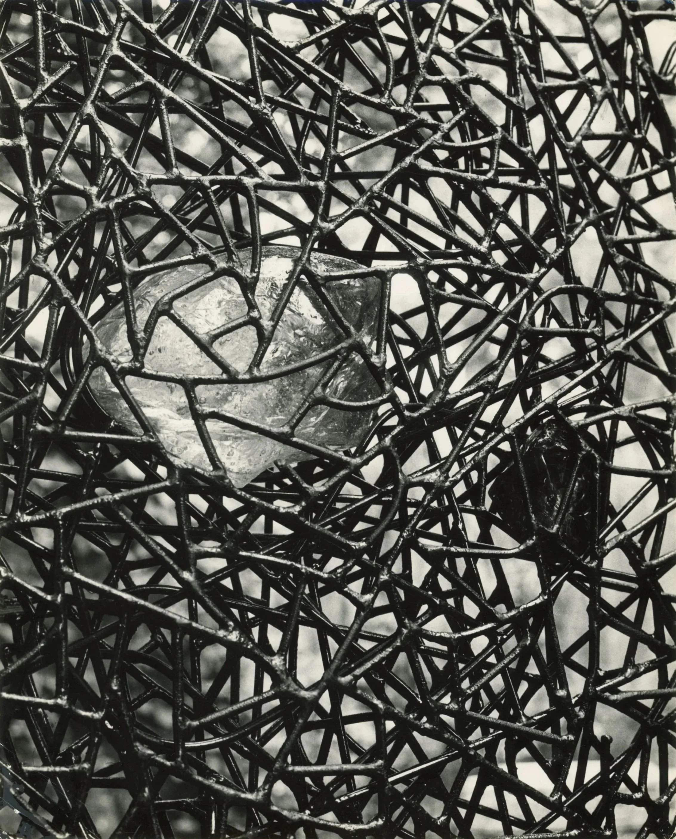 Black-and-white close-up of Claire Falkenstein's gates for the Peggy Guggenheim Collection, showing a dense, tangled metal web framing a large chunk of Venetian glass.