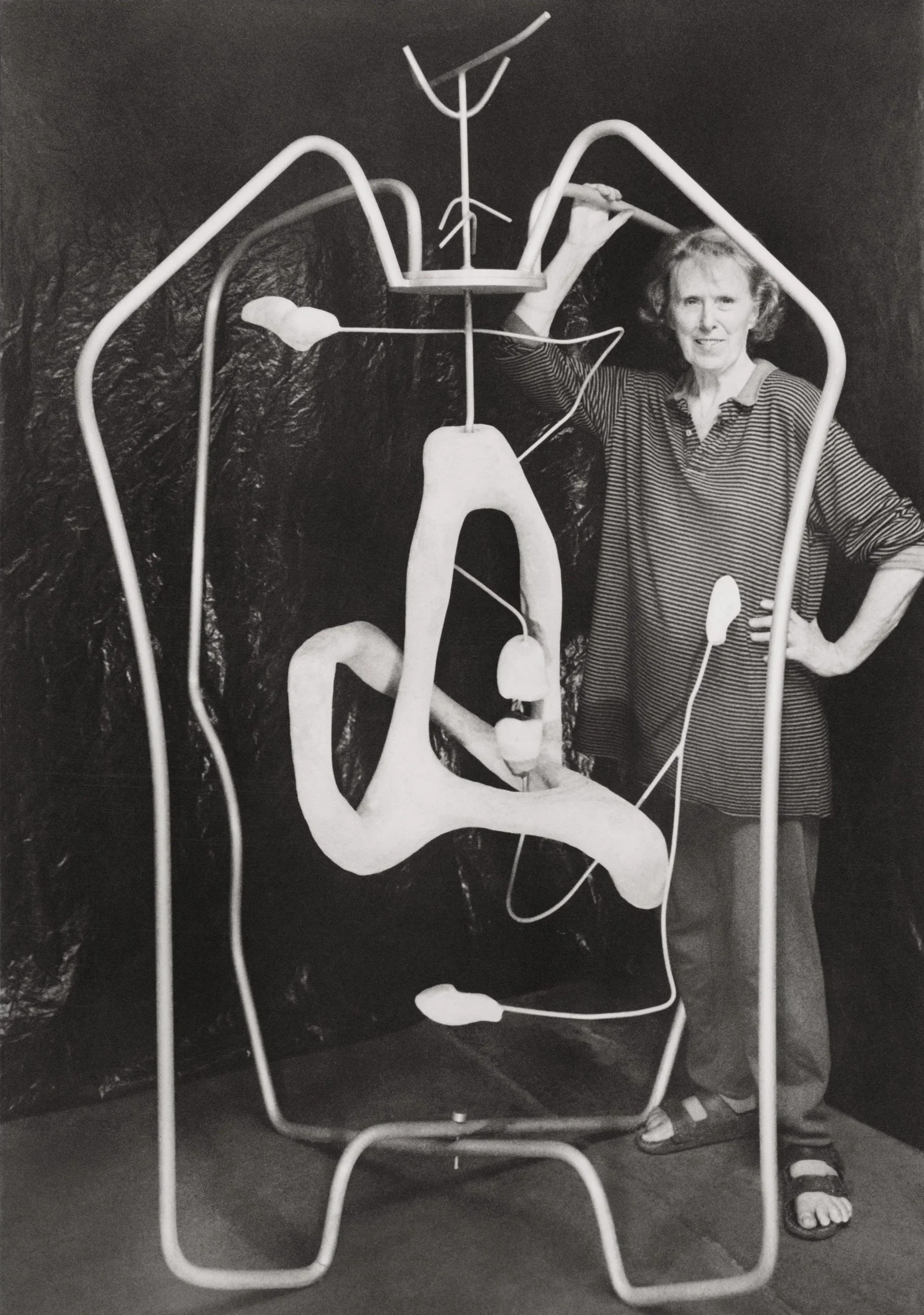 A black-and-white photograph of Claire Falkenstein standing within her oversized biomorphic sculpture, The Big Apple (1948).