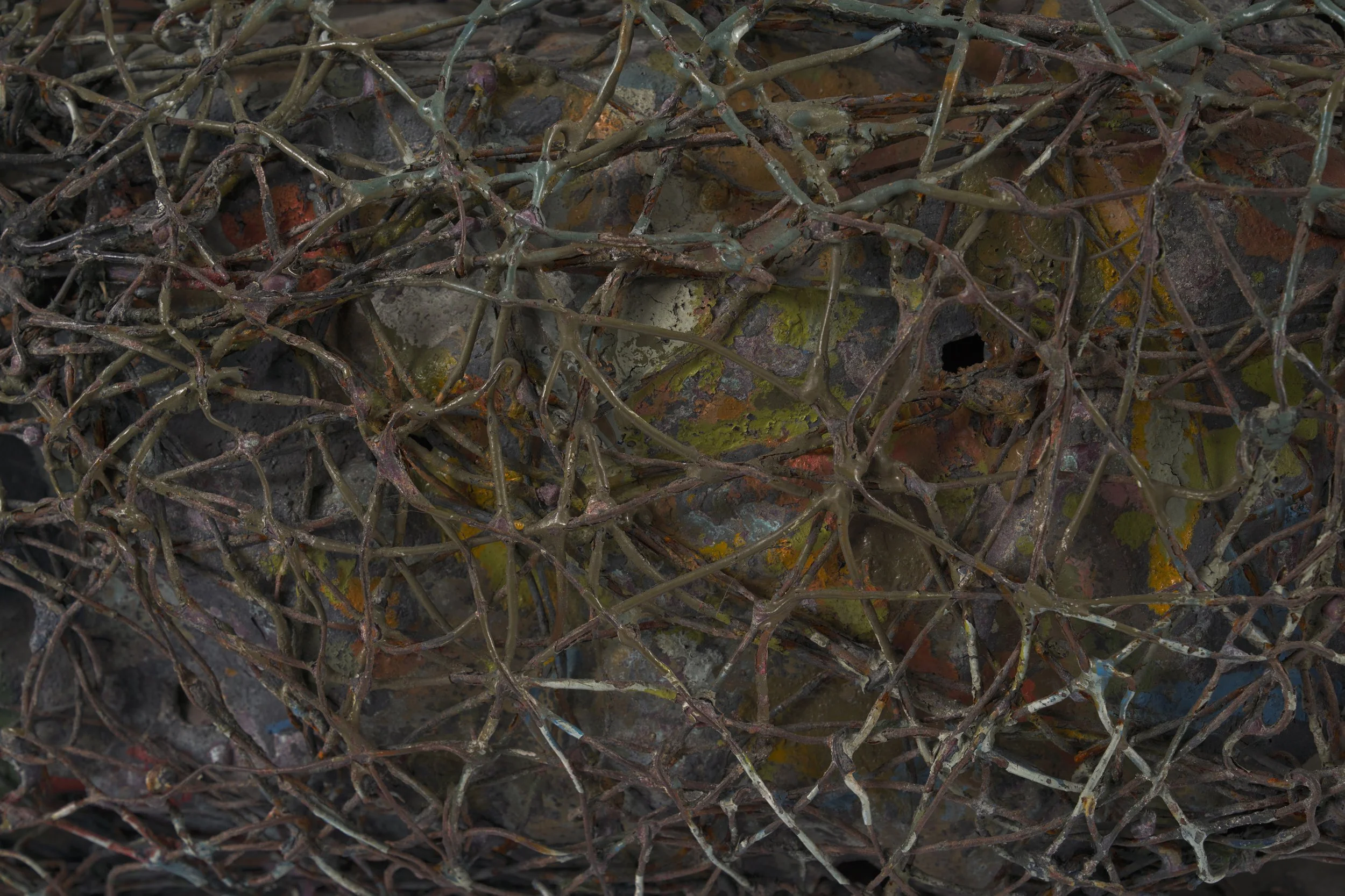 Close-up of a nest with intertwined twigs, sticks, and leaves covered in paint and debris.
