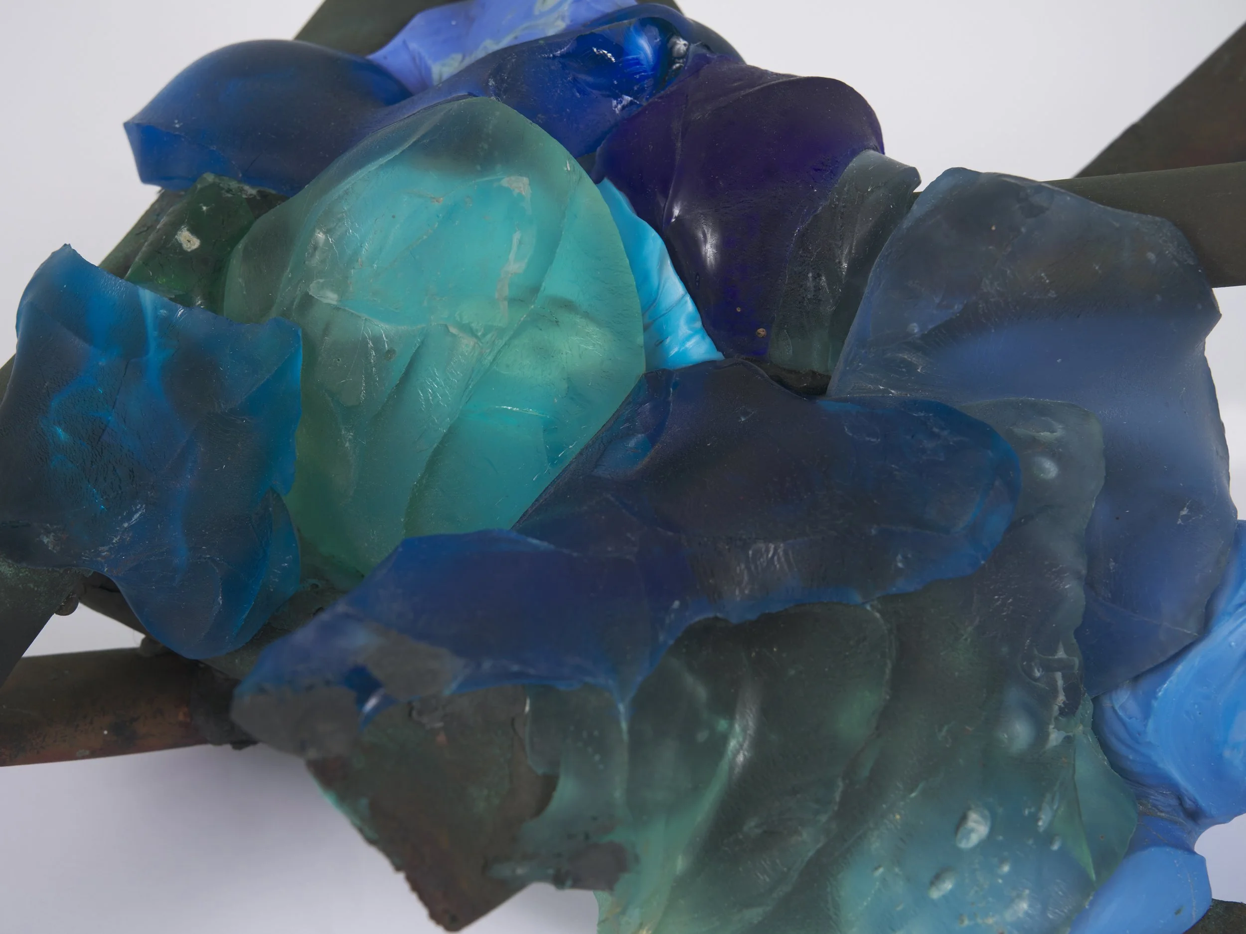 Close-up of colorful glass shards in shades of blue, green, and purple, placed on a dark surface.