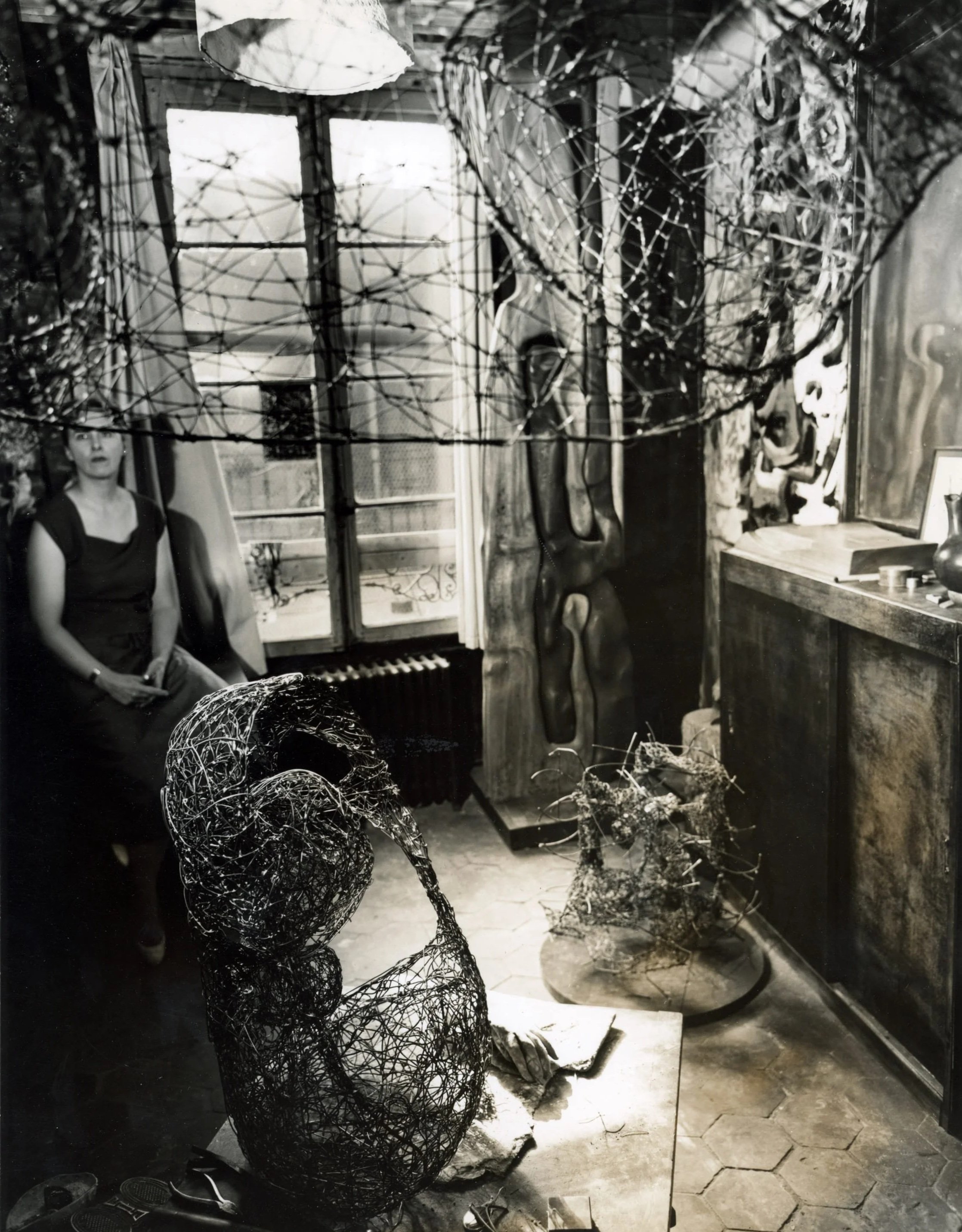 Black-and-white photograph of Claire Falkenstein in her Paris studio surrounded by numerous sculptures made of fused metal and wire.