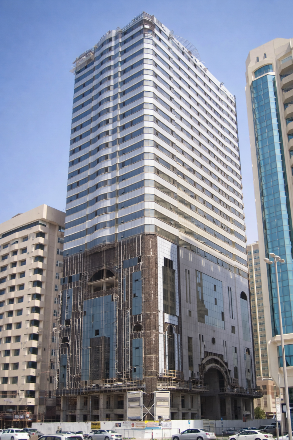 High-rise modern office building under construction, with glass windows and scaffolding at the base, surrounded by other tall buildings in an urban area.