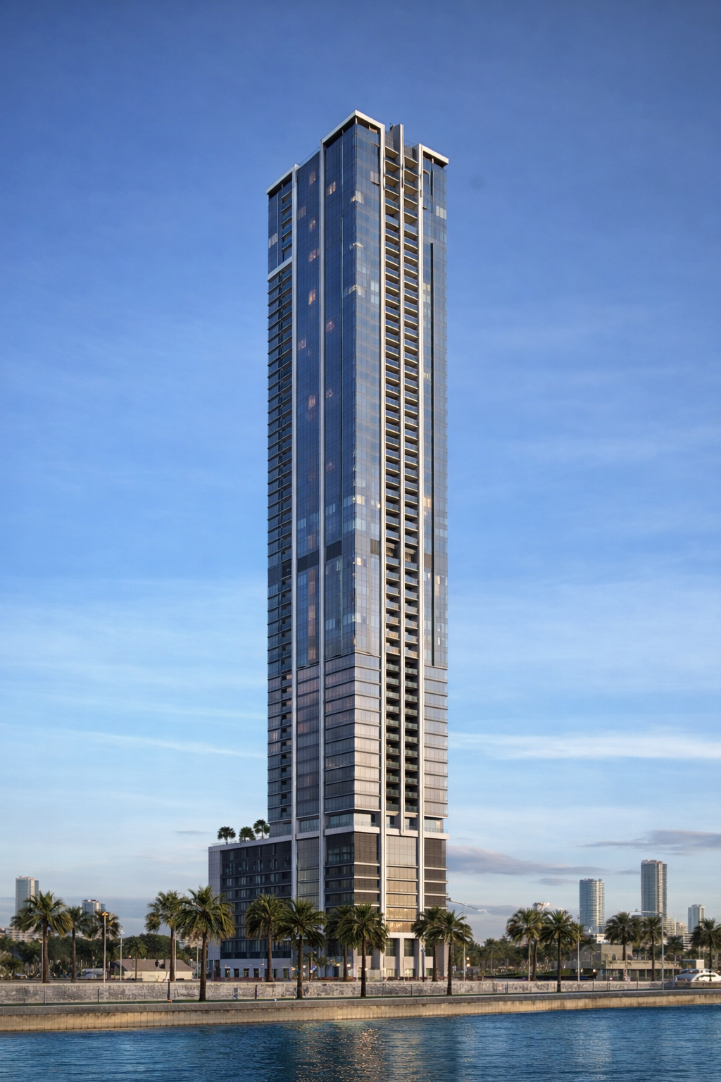 A tall modern skyscraper with glass windows and a white frame, situated near water with palm trees at its base, under a clear sky.