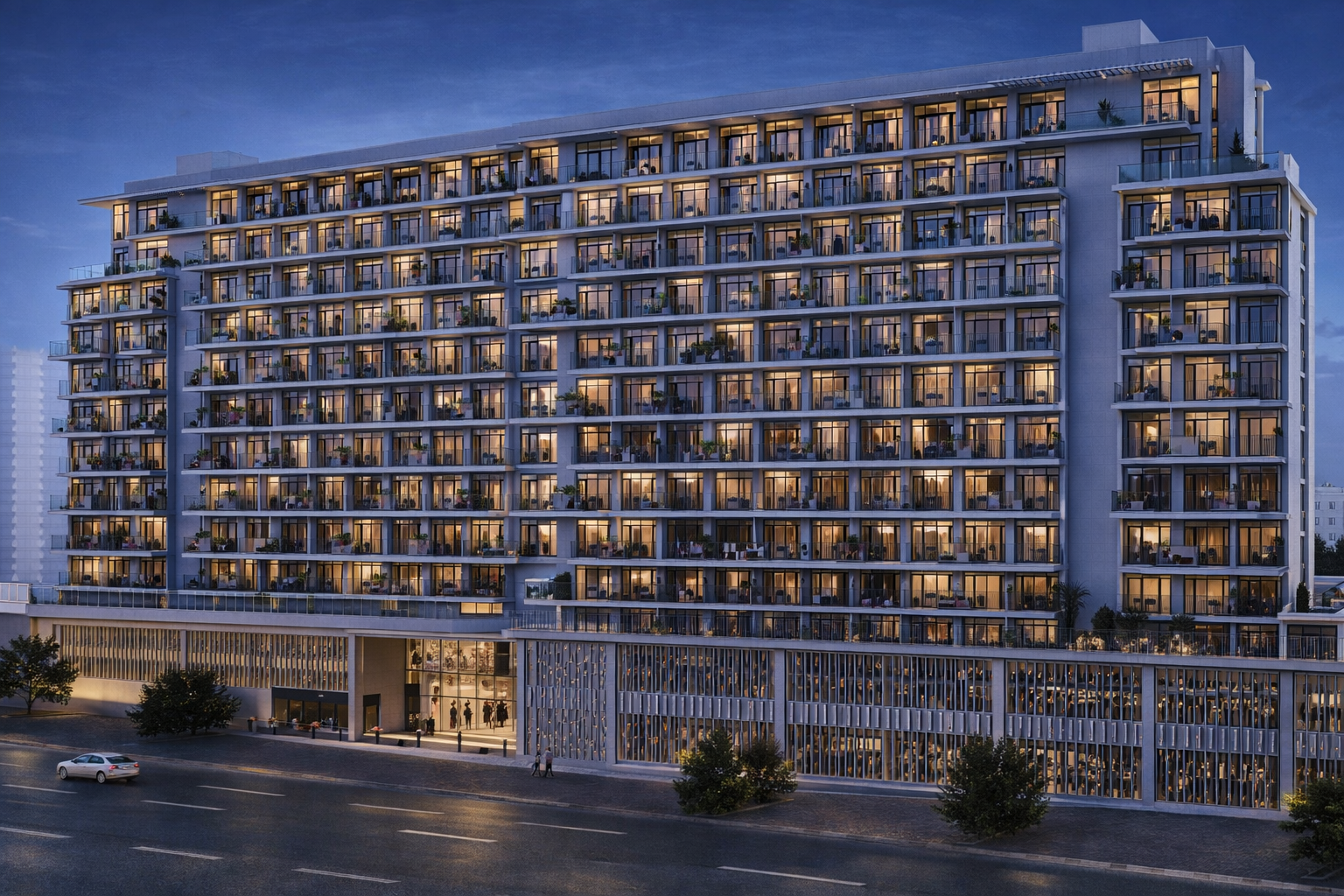 A modern multi-story residential building at dusk, with illuminated windows and balconies, situated along a city street with a few cars and trees.
