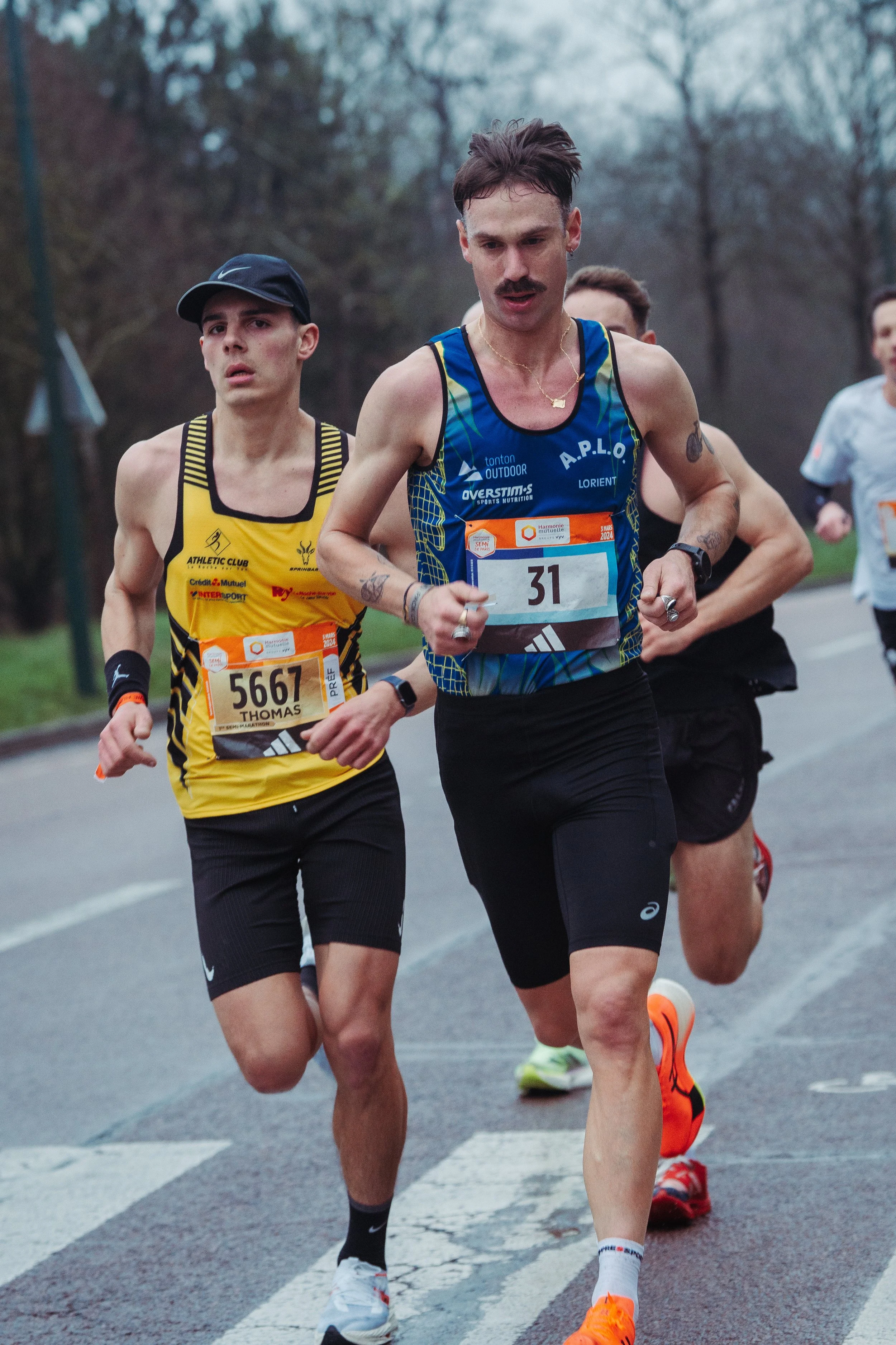 Groupe de coureurs participant à une course en extérieur sur une route pavée, portant des numéros d'identification.