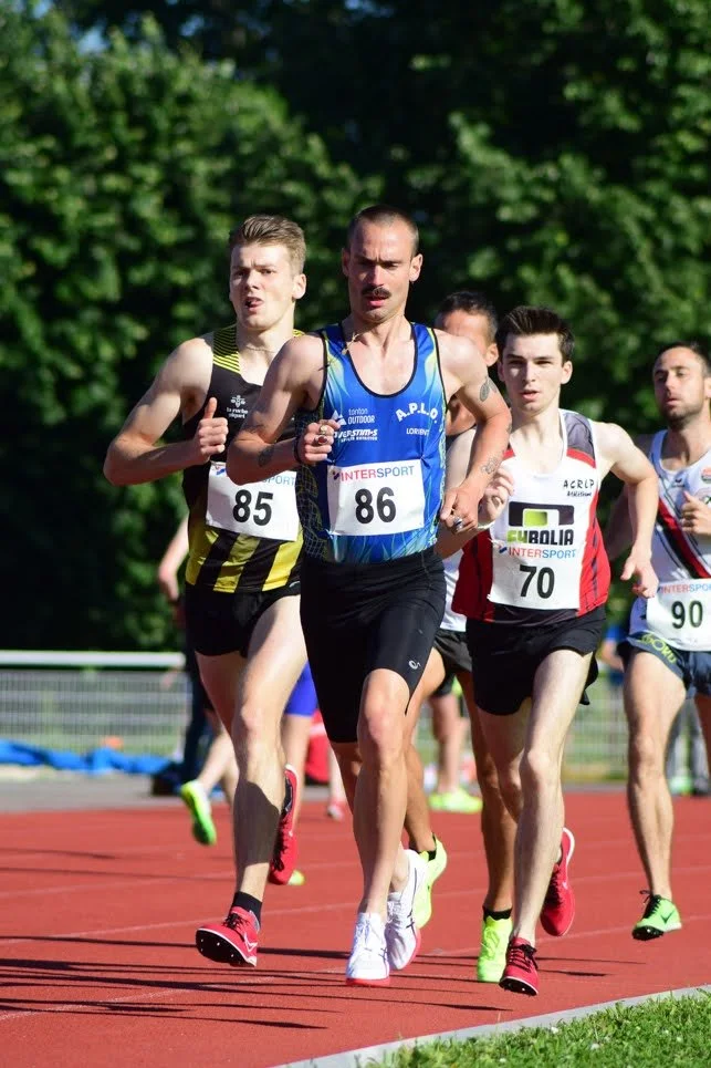 Des coureurs participent à une compétition de course sur piste, portant des vêtements de sport et des numéros.