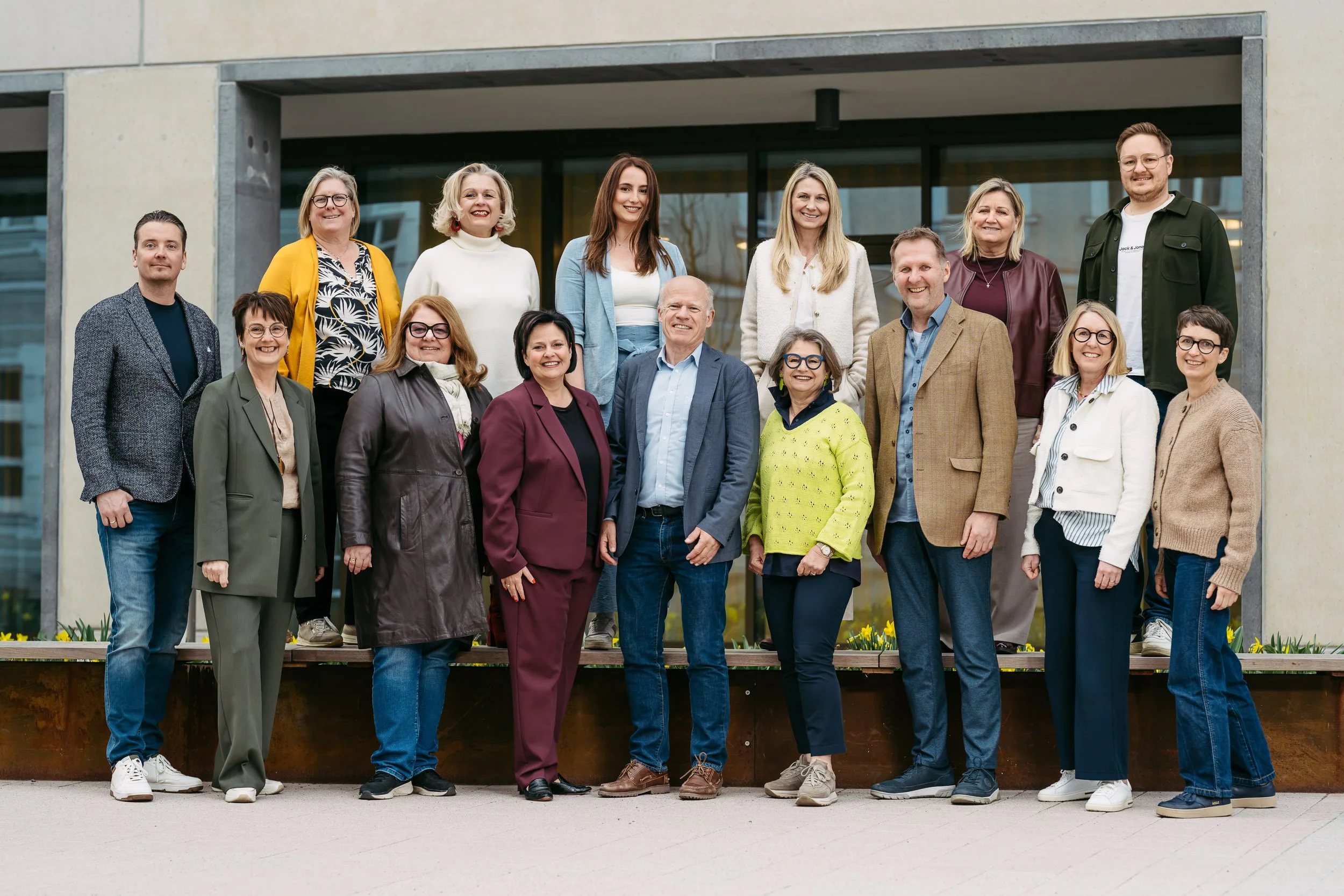 Gruppe von Menschen vor einem modernen Gebäude, lachend und posierend für ein Foto.