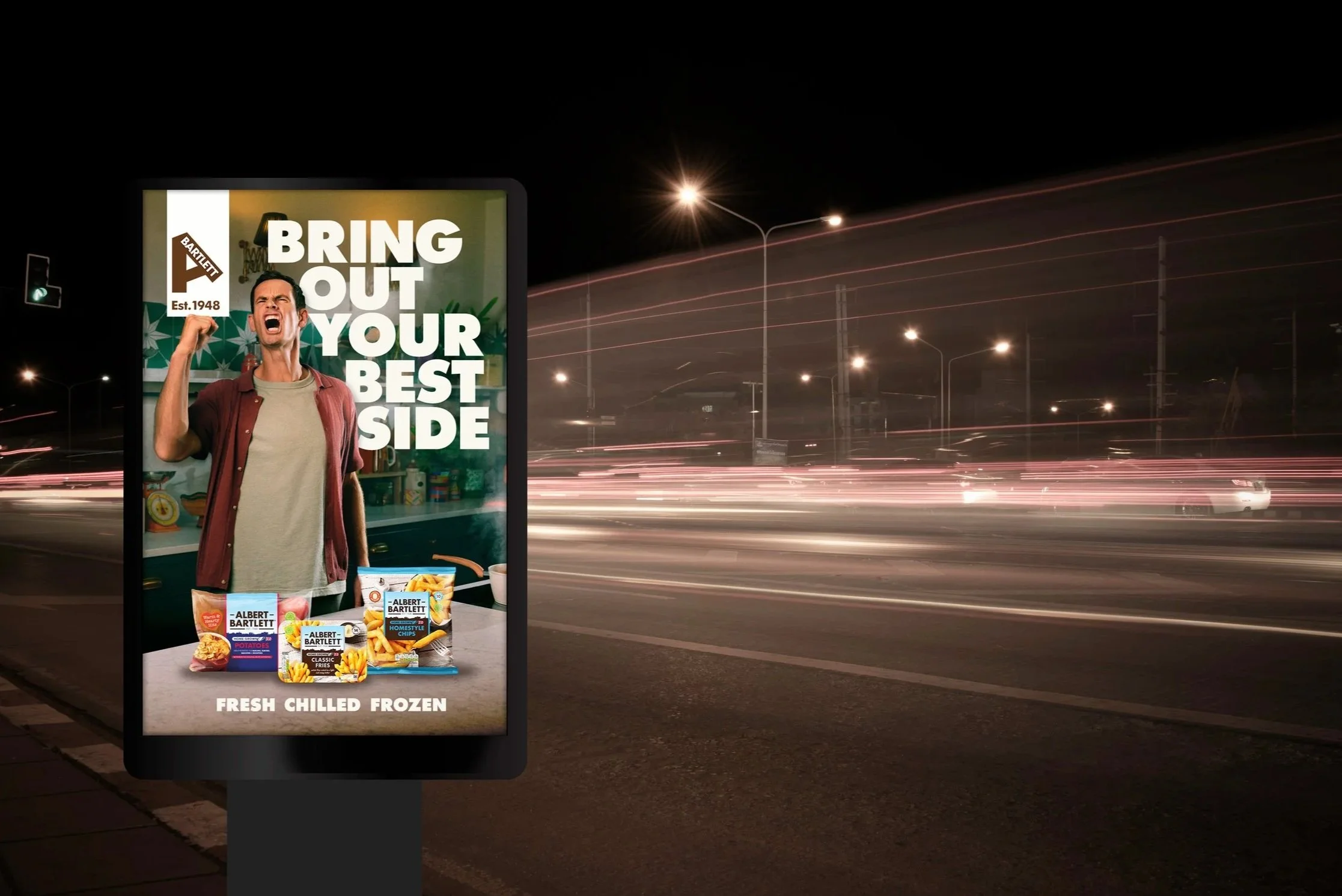 A digital billboard at night displaying an advertisement for Albert Bartlett frozen foods, with a man in a chef's coat shouting, and the text 'Bring out your best side'.