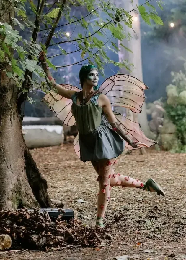 Fairy performer with butterfly wings and green makeup in forest during an immersive event experience