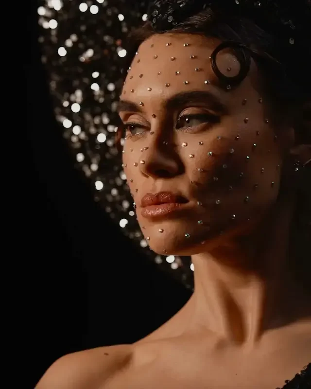 Performer with rhinestone face embellishments wearing a shimmering hat