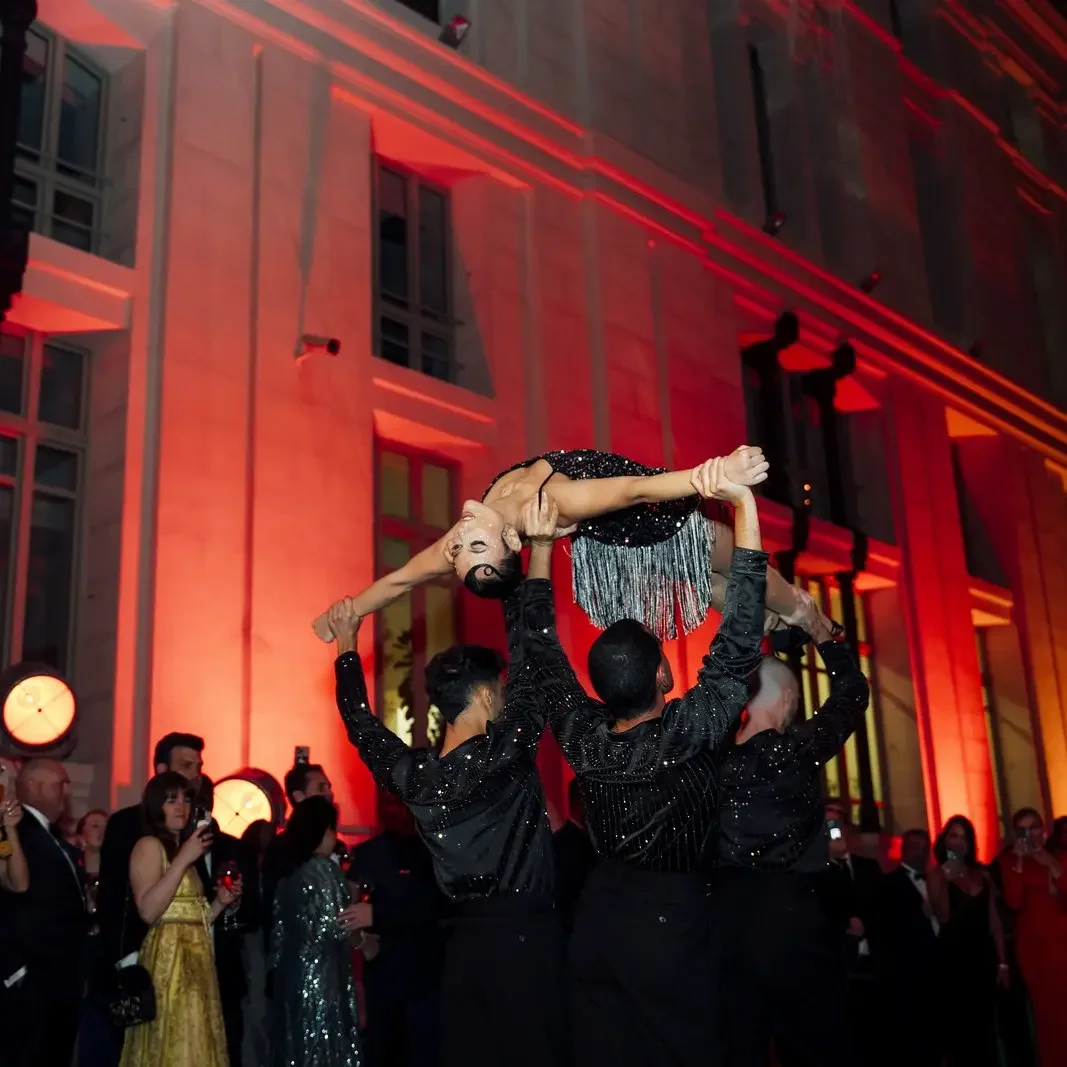 Dancers lifting performer in sparkly dress at elegant red-lit event