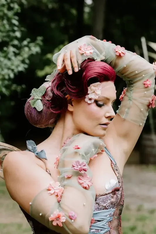 Fairy-inspired performer with pink hair and floral costume outdoors