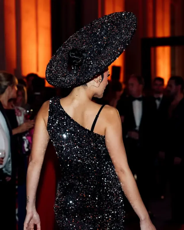 Performer wearing a sparkly black hat at a formal event with warm lighting