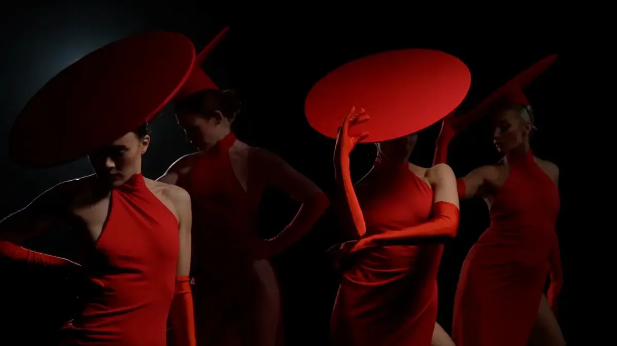Performers in red dresses and matching hats posing dramatically