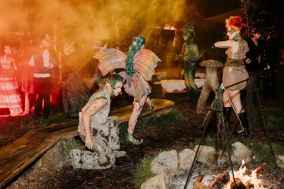 Fantasy-costumed performers gathered around campfire at nighttime woodland