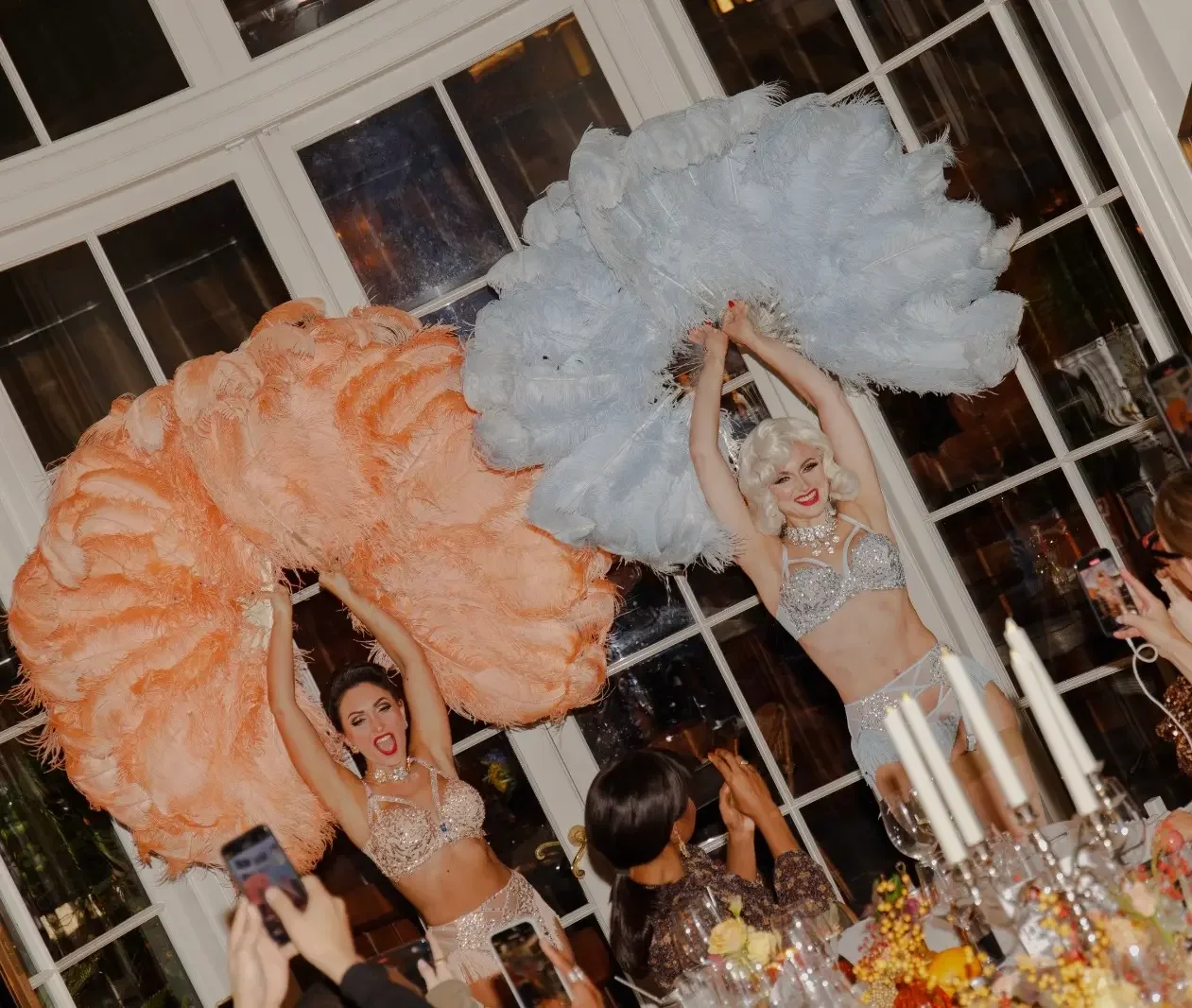 Glamorous performers with large feather fans on decorated table at premium event