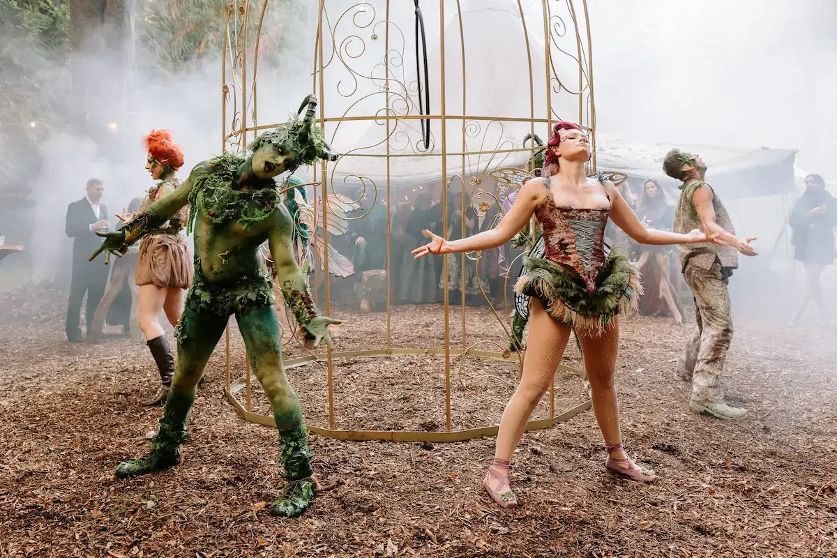 Fantasy performers posing around a decorated cage at an outdoor immersive experience