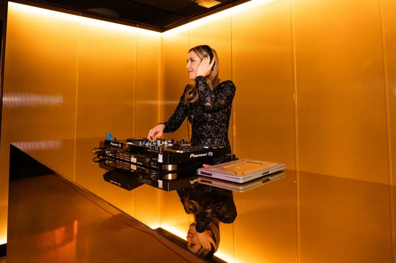 Female DJ in sequin dress mixing music in gold-toned luxury venue